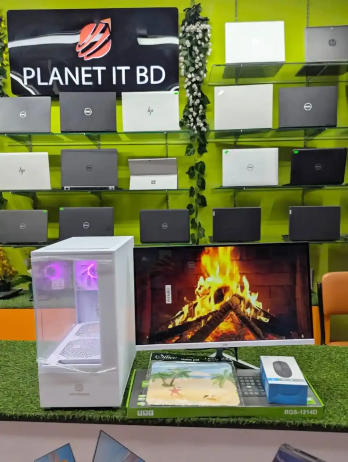 Wireless gaming PC setup with a transparent case and glowing fans, paired with a curved monitor displaying a fireplace on a gaming desk. Store interior showcasing laptops, accessories, and tech displays at Planet IT BD.